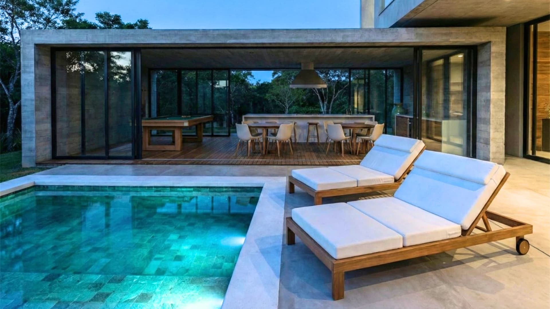 Área gourmet de luxo com bancada em ilha, mesa de sinuca e integração total com a piscina iluminada em casa contemporânea.