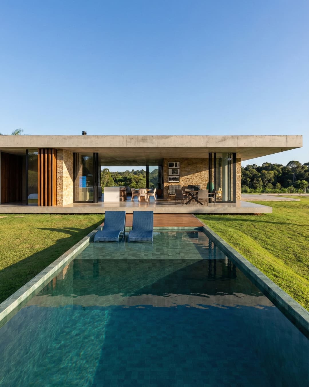 Piscina de borda infinita em casa de arquitetura contemporânea de alto padrão com fachada de concreto e pedra, projetada por arquiteto de luxo.