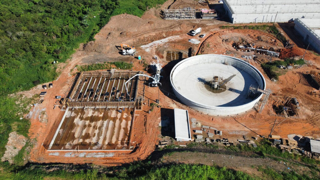 Obras de infraestrutura urbana de saneamento com tubulações, escavações e equipamentos de grande porte.