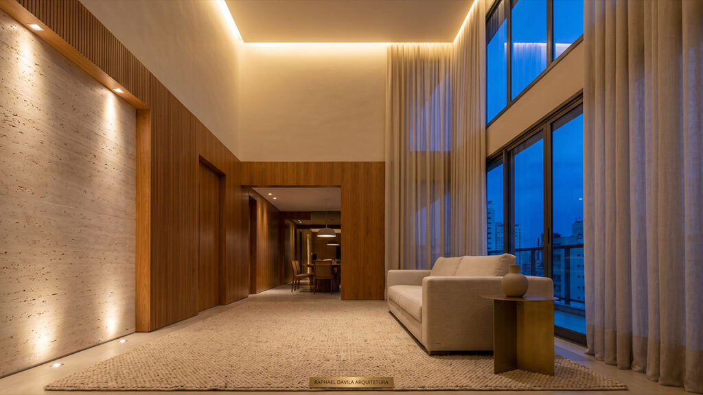 Sala de estar de alto padrão com pé-direito duplo, parede em travertino, painéis de madeira e iluminação embutida ao entardecer.