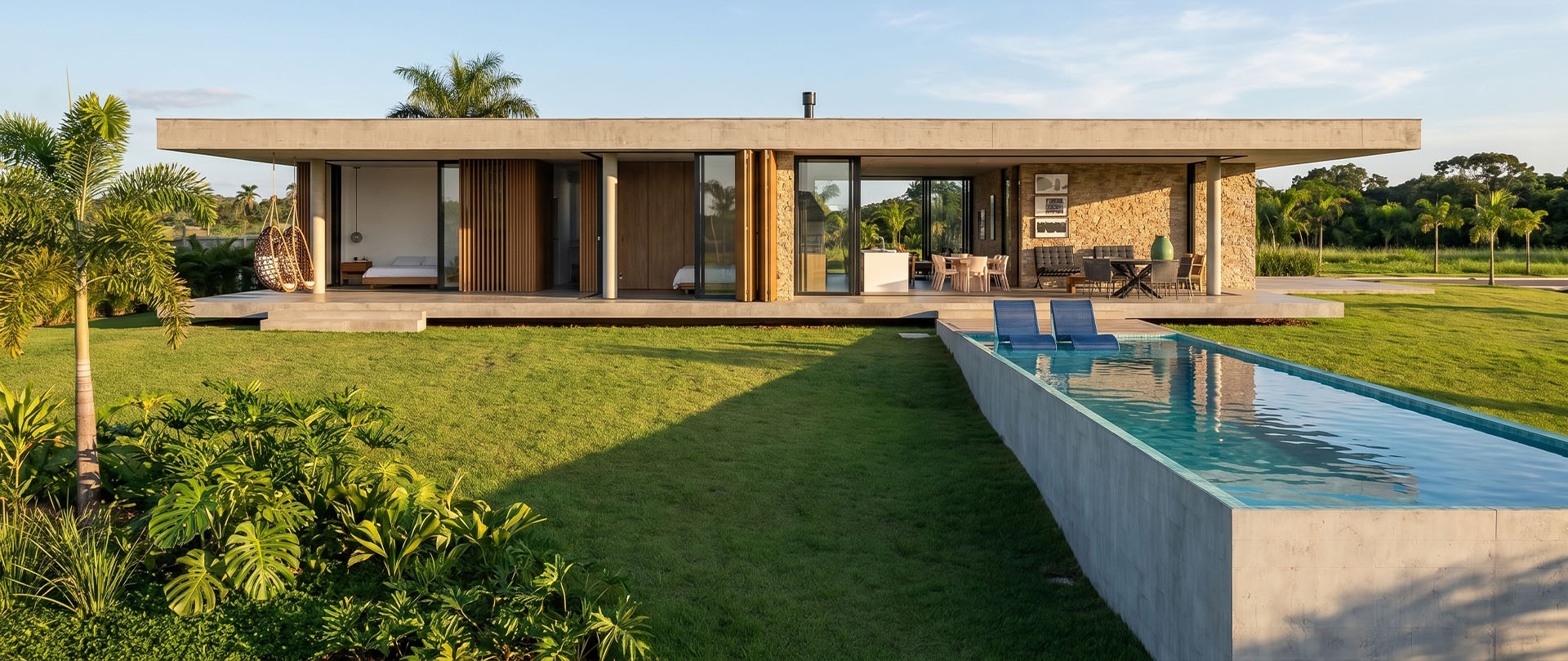 Casa térrea com laje de concreto aparente, painéis de madeira, parede de pedra e piscina elevada. Projeto de Raphael Davila